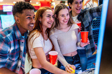 Happy multiethnic friends playing arcade games and enjoying weekend together