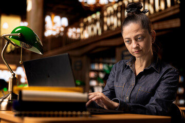 Fototapeta premium Professional author and librarian working on her laptop in a public library, focused on providing academic resources and guidance. Evaluating educational information within the database.