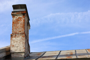Old Weathered Brick Chimney With Peeling White Paint On A Rusty Metal Roof Against A Blue Sky With...
