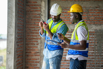 Two engineers measuring and inspecting electrical conduit installation on a brick wall at a construction site. Quality assurance and infrastructure development process.