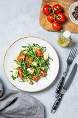 Arugula salad with cherry tomatoes, mozzarella and pesto sauce on a light background
