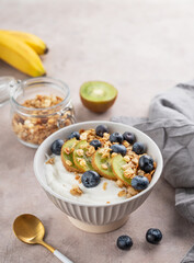 Natural greek yogurt with granola, kiwi and blueberries in a bowl on a light background