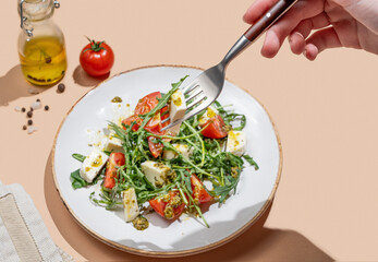 Hand holding fork fresh arugula salad with cherry tomatoes, mozzarella, pesto sauce