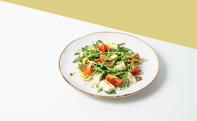 Fresh arugula salad with cherry tomatoes, mozzarella, pesto sauce on white yellow background