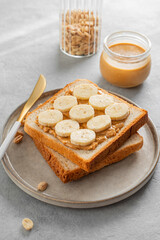 Peanut butter toast with banana on a plate on a light background with morning shadow.
