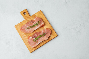 Freshly prepared meat on a wooden cutting board with herbs in a kitchen