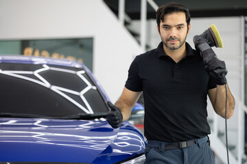 Professional car detailer wearing black gloves and a black polo shirt polishes a blue vehicle using...