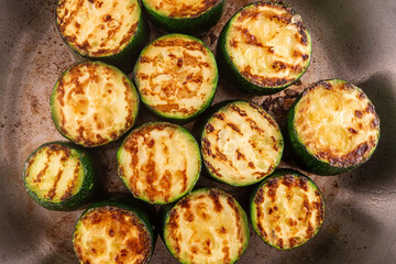 Close-up overhead view of rustic zucchini pieces searing in a stainless steel frying pan, showcasing perfect caramelization and charred edges