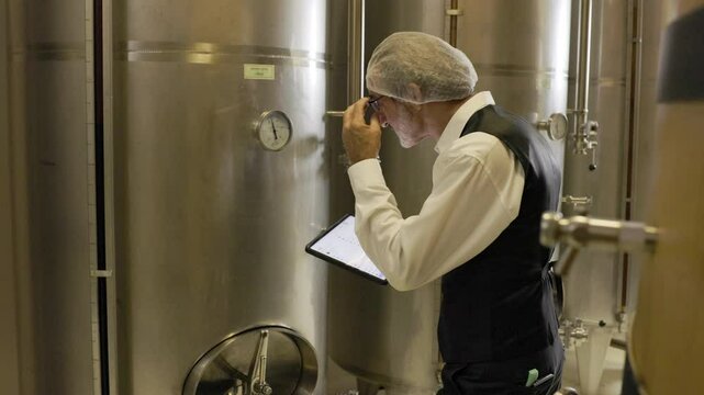winemaker : professional winemaker working inspection process of make wine at modern wine factory rolls barrel.  stainless wine barrels or cognac barrels in the cellar of the winery