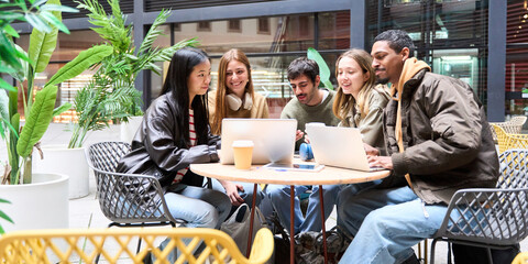 multiethnic University students collaborating on project using laptops in cafe courtyard