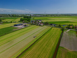 Aerial view of a Dutch rural landscape with green fields, a tractor working on the land, farm...