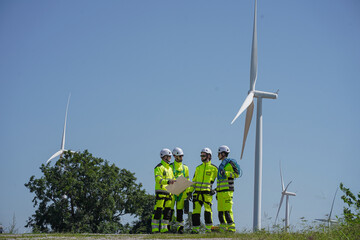 Maintenance engineer team standing at windmills at wind turbine farm. Group of people wear safety...