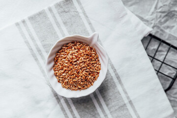 Flaxseeds in a small bowl placed on a kitchen towel with a wire rack background