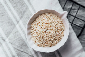 Sesame seeds in a small dish on a textured surface in a kitchen setting