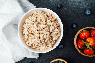 Healthy oatmeal bowl with fresh strawberries and blueberries on a dark surface