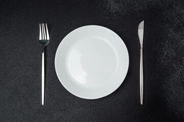 Cutlery arranged neatly beside a white plate on a dark surface