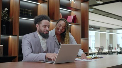 In a stylish office designed for collaboration, a businessman reviews work on his laptop while a supportive colleague shares valuable insights and creative ideas to enhance the project