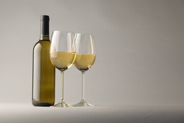 Tasty white wine in glasses and bottle on light grey background, space for text