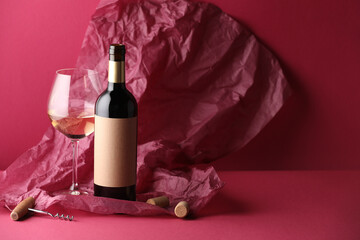Bottle and glass of wine with corkscrew, corks and paper on crimson background. Space for text