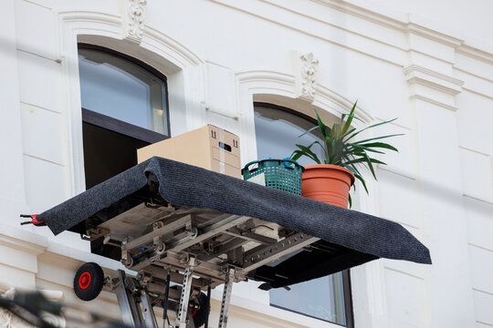 Mover service lifting ladder cargo crane platform cardboard box plant pot city street. Retractable furniture elevator machine car pickup truck rental company for relocation and house moving delivery