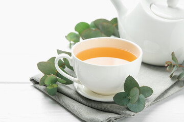 Aromatic tea in cup and eucalyptus branches on white wooden table, closeup