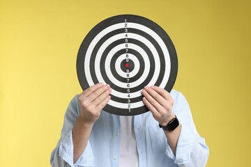 Targeting. Man with dart board on yellow background