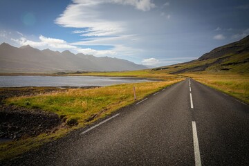 Lonely Icelandic road stretching through moody land under a sunny sky