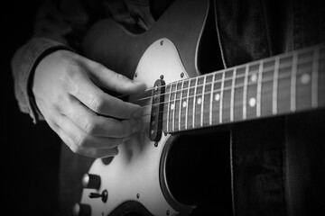 Fototapeta premium Man playing guitar in darkness, closeup. Black and white effect