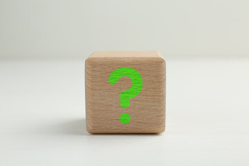 Wooden cube with question mark on light grey background, closeup