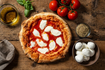 Round pizza with tomato sauce, mozzarella, basil, and oregano, top-down view on a rustic wooden surface. Traditional Italian dish made with fresh and simple ingredients.