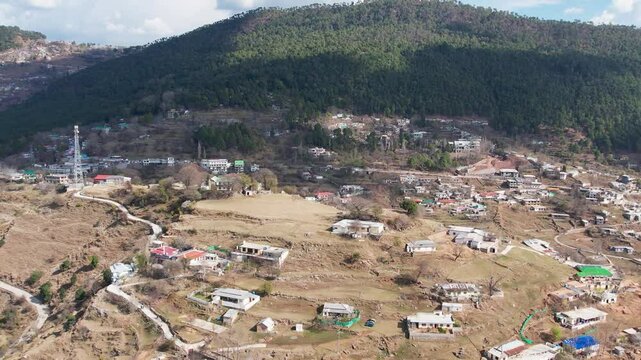 hillside homes, terraced fields, and a mobile tower in Murree under clear winter skies. Murree, Pakistan