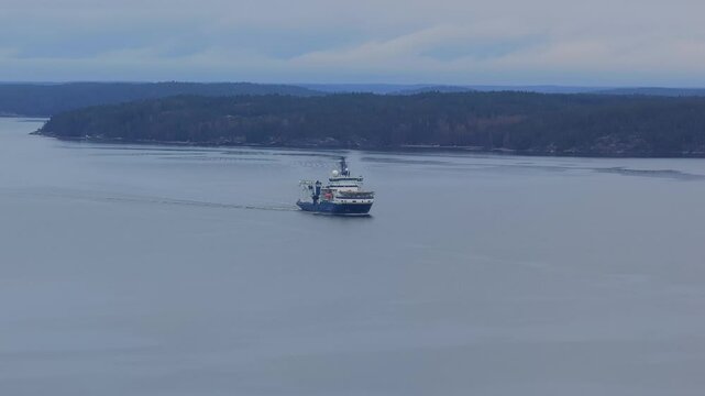 Multipurpose offshore support vessel and Ice breaker moving ahead in Finnish archipelago. Calm overcast weather. Distant aerial view.