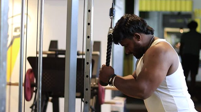 Tricep pushdown exercise in a gym by a man wearing a sleeveless to improve triceps. Tricep pushdown to build stronger arms