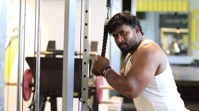Tricep pushdown exercise in a gym by a man wearing a sleeveless to improve triceps. Tricep pushdown to build stronger arms