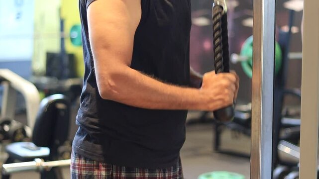 Tricep pushdown using rope exercise in a gym by a man wearing a black t-shirt to improve triceps. Tricep pushdown to build stronger arms