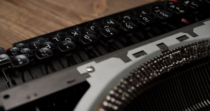 Close-up of a black vintage typewriter keyboard with white QWERTY keys. Slightly blurred lower keys create depth, red trim accents, wooden background. Elevated angle.