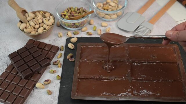 Preparing Stacked layers of kadaif embrace a generous coating of rich chocolate and are topped with a pistachio, showcasing the delightful texture and flavors in a culinary presentation.