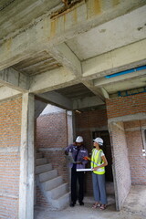 Two male and female foremen, construction engineers supervise construction of a house, black construction manager and female engineer inspect the work holding walkie-talkies in a real estate 