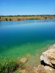 Peaceful lake shoreline with clear turquoise water and blue sky.