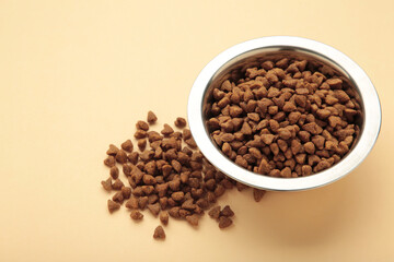 Dog or cat dry food in a silver bowl on beige background. Space for text