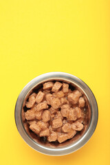 Wet pet food in feeding bowl on yellow background. Vertical photo