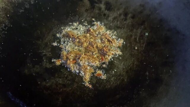 Asian cook is cooking in thai kitchen in local traditional country style, preparing sizzling thai green curry paste being stir fried in traditional wok to cook thai food green curry popular worldwide