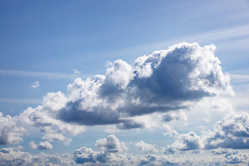 Large silver lined white clouds floating in a brightly lit sunny blue sky.