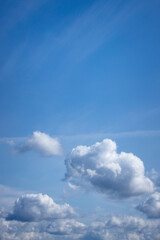Portrait of white puffy clouds floating in a blue sky.