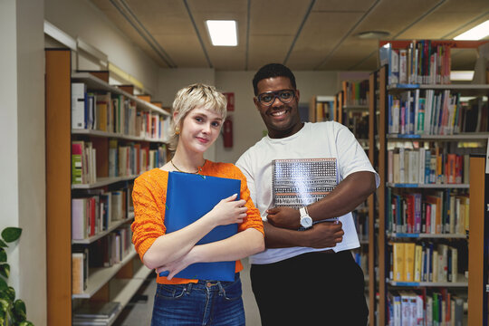 Confident university students posing in library with folders
