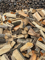 Chopped firewood in front of a stacked log wall. Split wood ready for use as firewood or heating fuel. Close-up outdoor view.