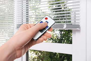 Woman using remote to control blinds in room, closeup