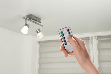 Woman using remote to control lighting in room, closeup