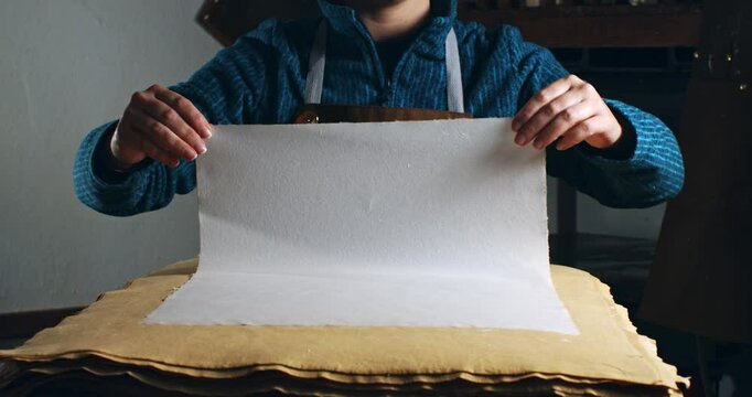 Super Slow Motion of Handmade Paper Sheet Being Carefully Handled on a Wooden Surface, Showcasing Its Texture, Deckled Edges, and Natural Imperfections in a Craft or Artistic Studio Environment.