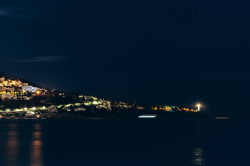Night view of the Saint-Jean-Cap-Ferrat lighthouse shining on the peninsula, with illuminated villas along the coastline.